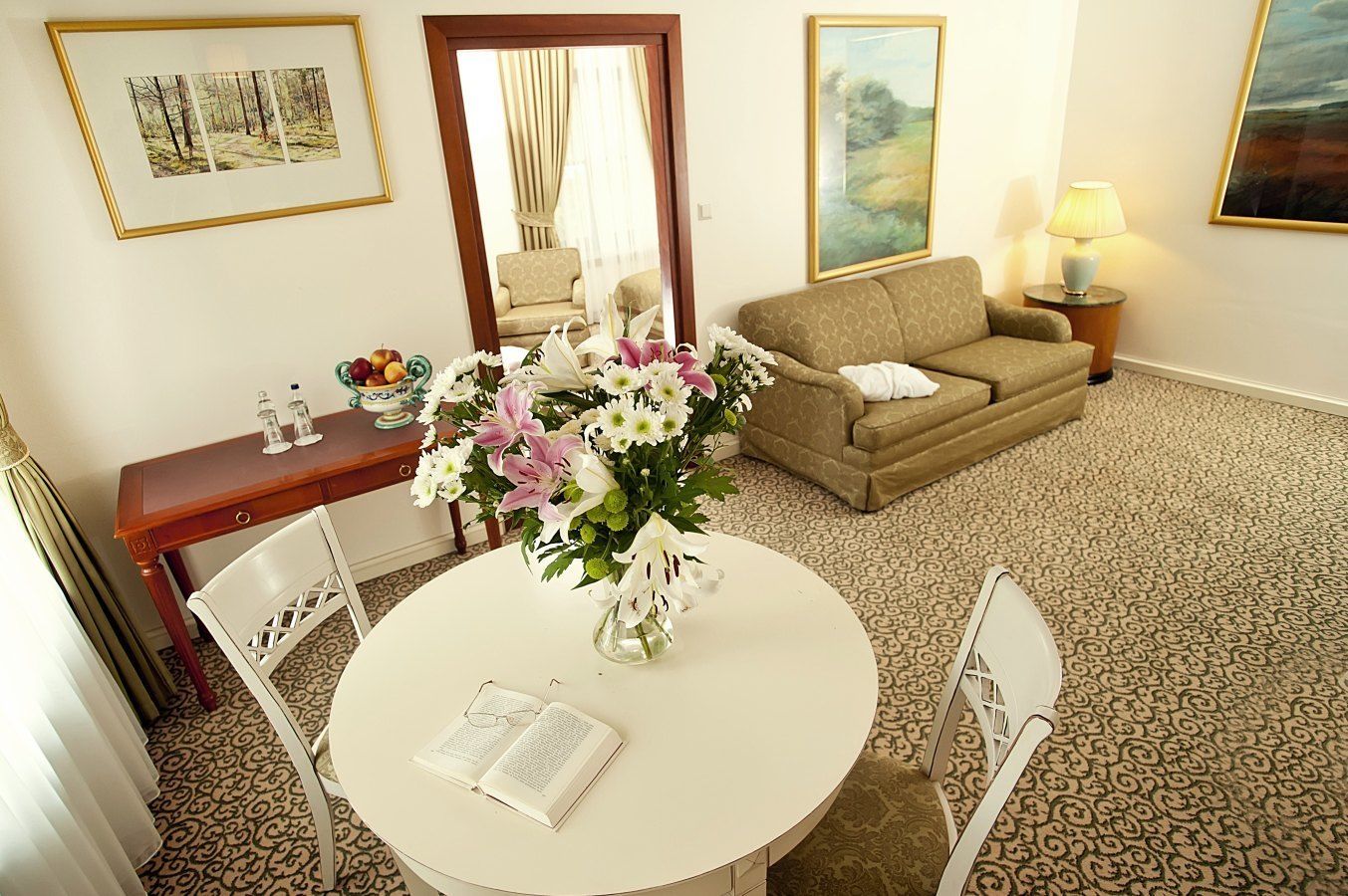 Una habitación de hotel con una mesa redonda, un sofá, un espejo y una lámpara.