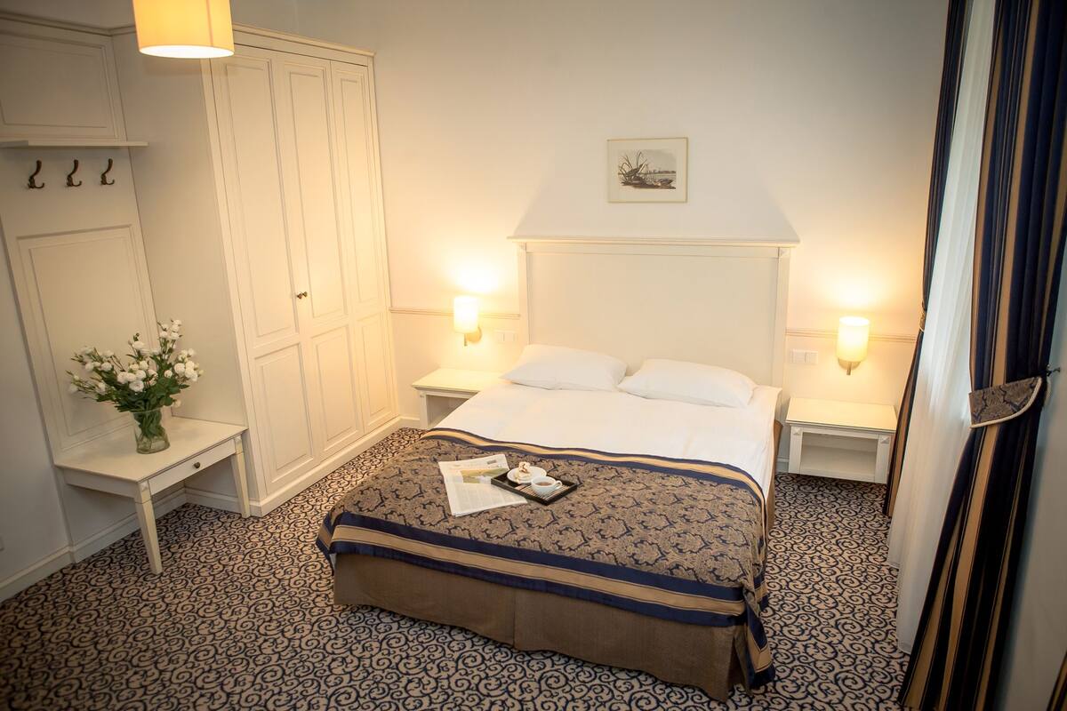 Une chambre d’hôtel avec un lit, des tables de chevet, une commode, une armoire et un tableau au mur.