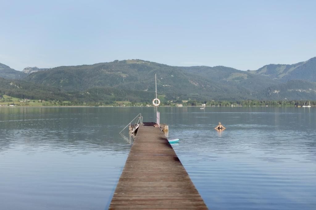 A wooden pier extending into a calm lake with mountains in the background.