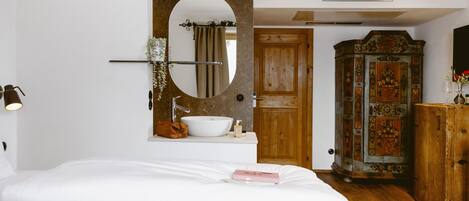 A bedroom with a large bed, a round mirror, a white sink, and a wooden wardrobe.