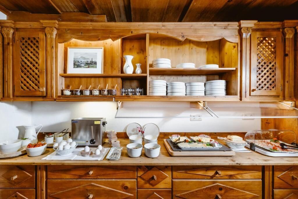 A wooden kitchen with shelves holding plates and bowls, a coffee maker, and a refrigerator.