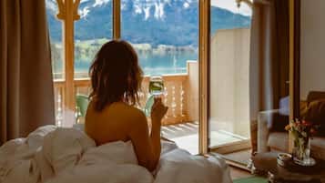 Una persona sentada en una cama con vistas a una montaña y un lago a través de una puerta de cristal.