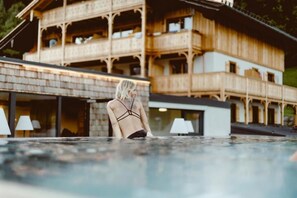 A person in a swimming pool with a wooden building in the background. - Berau Landhotel am See (Sankt Wolfgang im Salzkammergut)