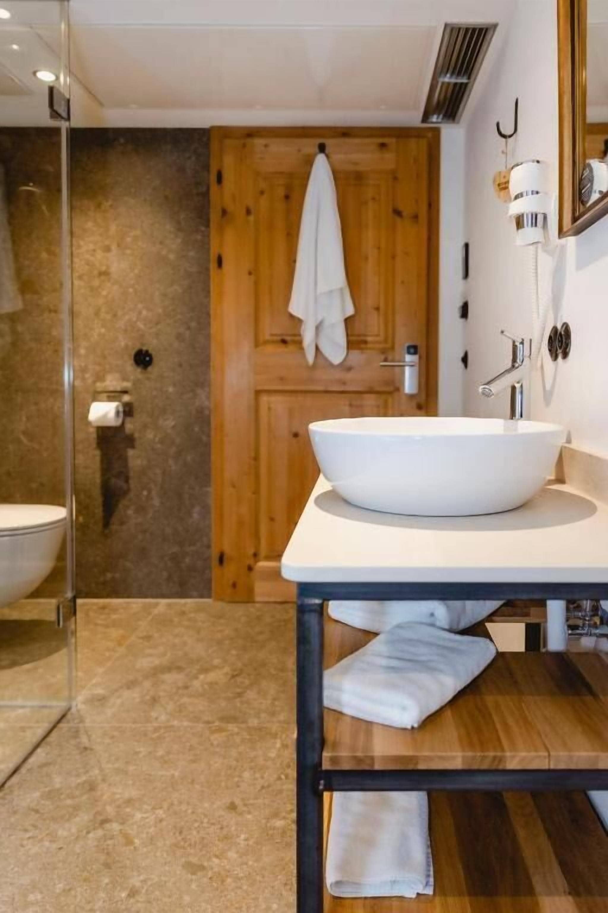 A bathroom with a large white sink, wooden door, and a towel rack.