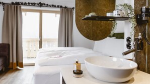 Habitación de hotel con una cama grande, un lavamanos blanco con un recipiente amplio, un espejo y un secador de pelo fijado en la pared.