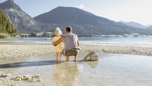 Una pareja de pie en una playa de guijarros con una montaña al fondo.