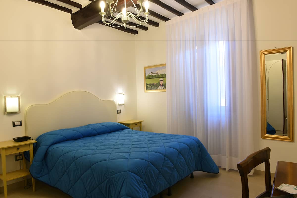 A bedroom with a large bed, bedside tables, a nightstand, a chair, a mirror, and a painting on the wall.
