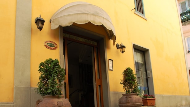 A yellow building with a large arched entrance, two potted plants, and a red doormat. - Albergo Ristorante Umbria (Città di Castello)