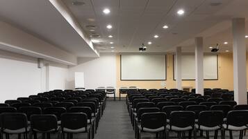 Uma sala de conferências com fileiras de cadeiras, uma tela de projetor e um quadro branco.
