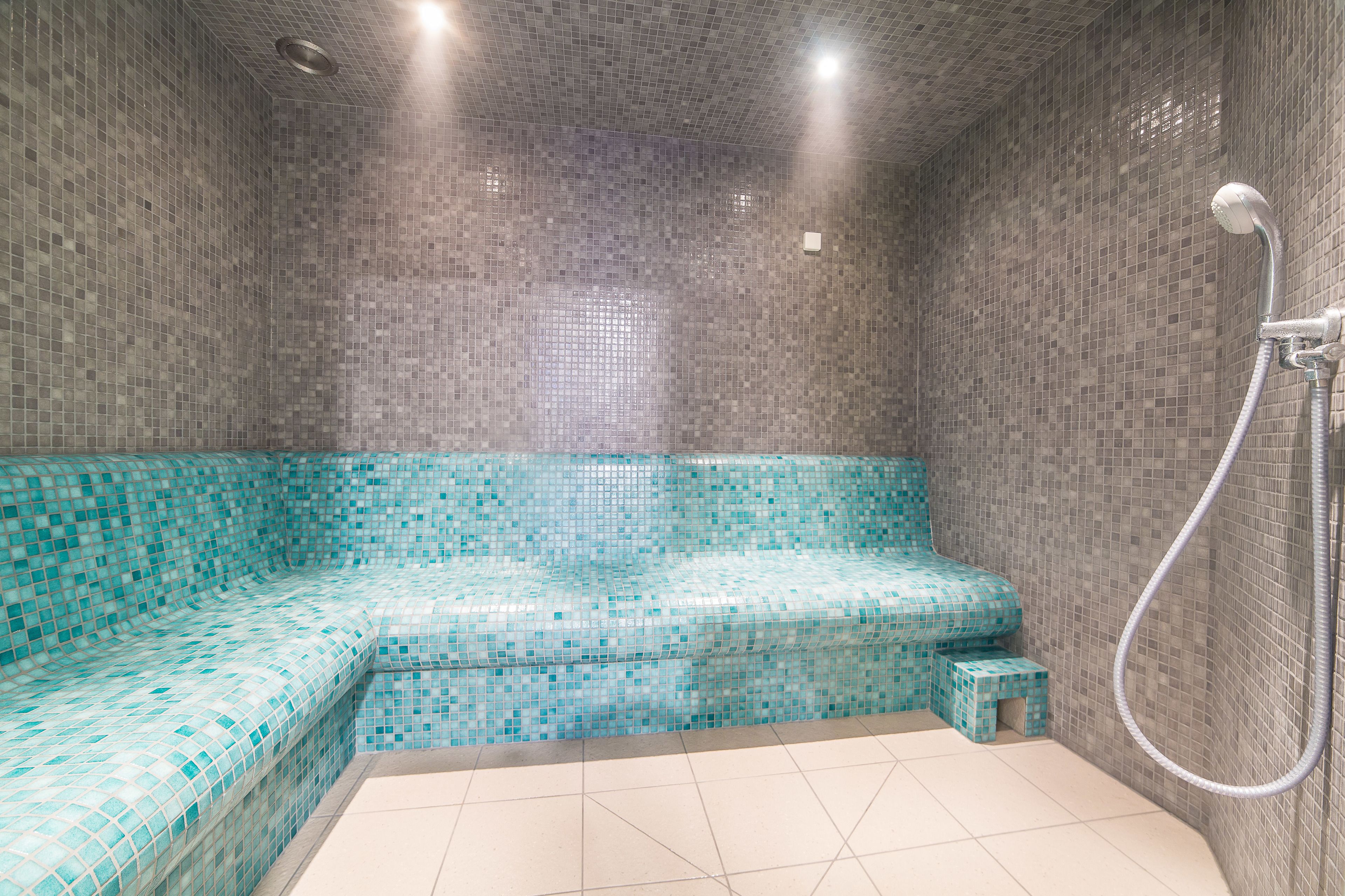 Un baño con zona de ducha revestida de mosaicos y lavamanos en esquina.