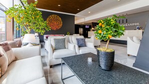 Een moderne hotel lobby met een receptiebalie, zithoek en decoratieve planten.