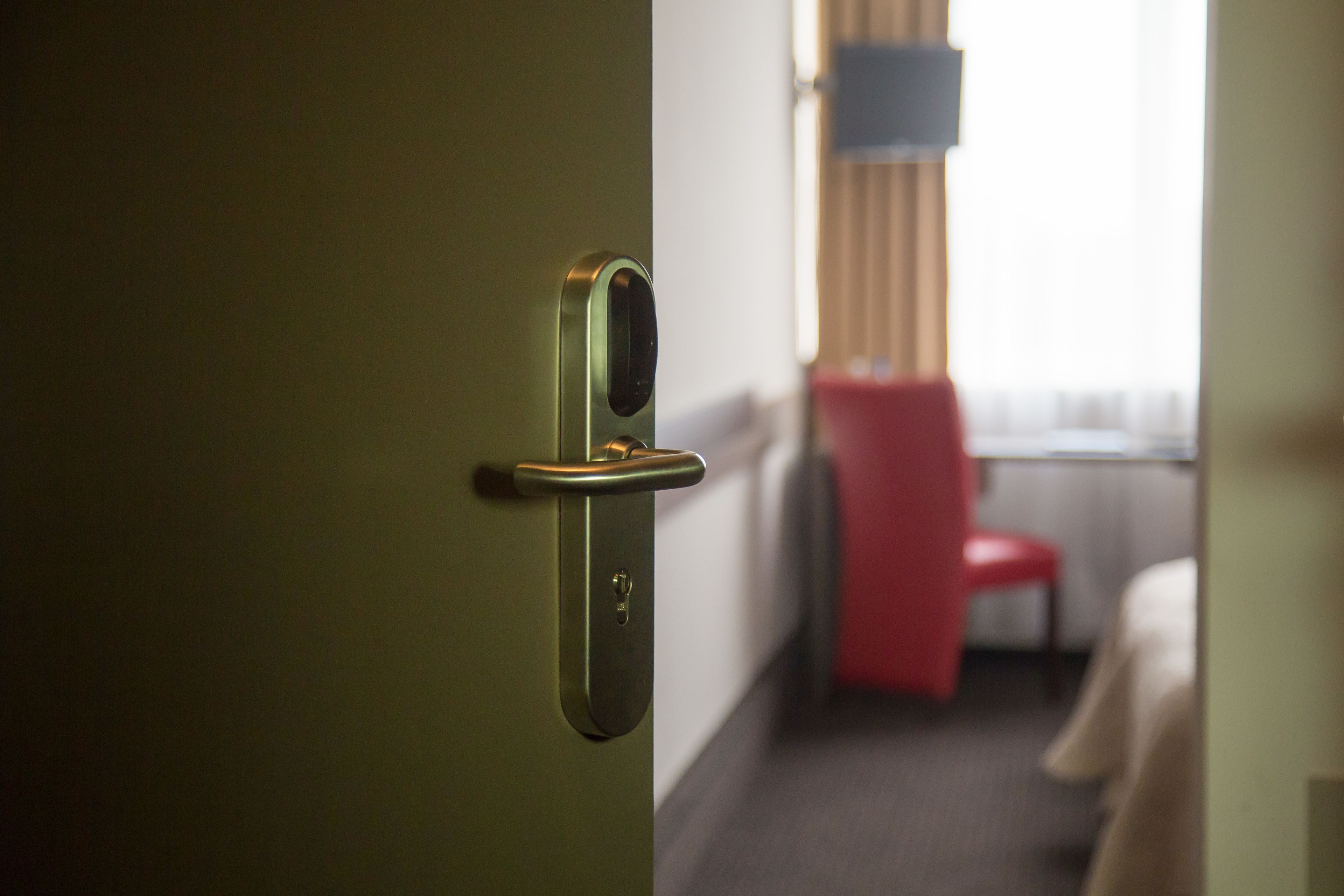A hotel room with a door, a red chair, and a bed.