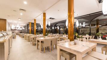 Un restaurant spacieux, doté de nombreuses tables et chaises, de grandes colonnes dorées et d’un éclairage moderne suspendu au plafond.