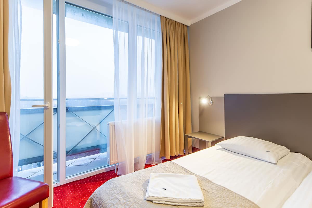Une chambre d’hôtel comprenant un lit, une chaise, une table de chevet et une vue sur l’extérieur grâce à une porte-fenêtre coulissante.