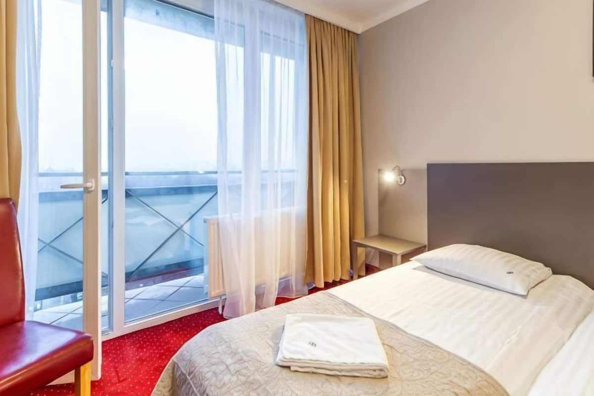 Une chambre d’hôtel avec un lit, une chaise, une table de chevet et une vue sur l’extérieur, accessible par une porte-fenêtre coulissante.