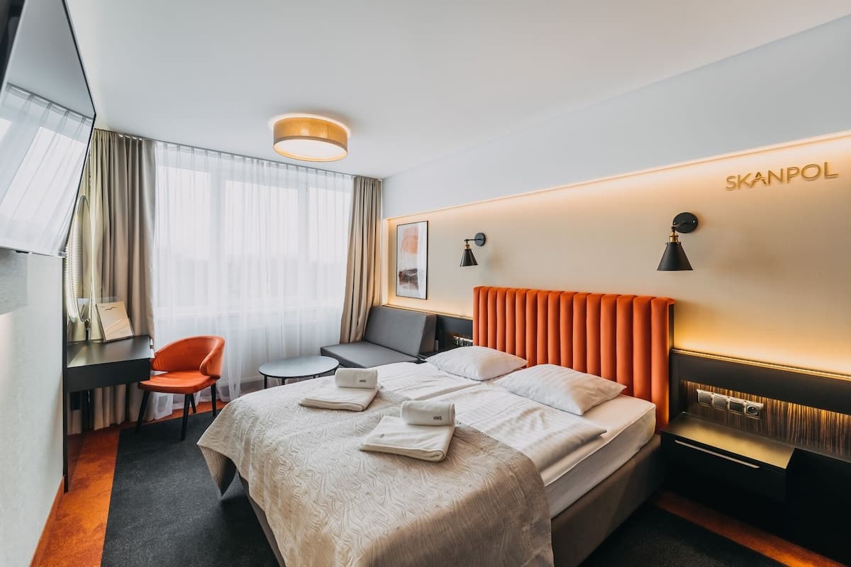 Une chambre d’hôtel équipée d’un lit, d’un bureau, d’une chaise et d’une lampe fixée au mur.