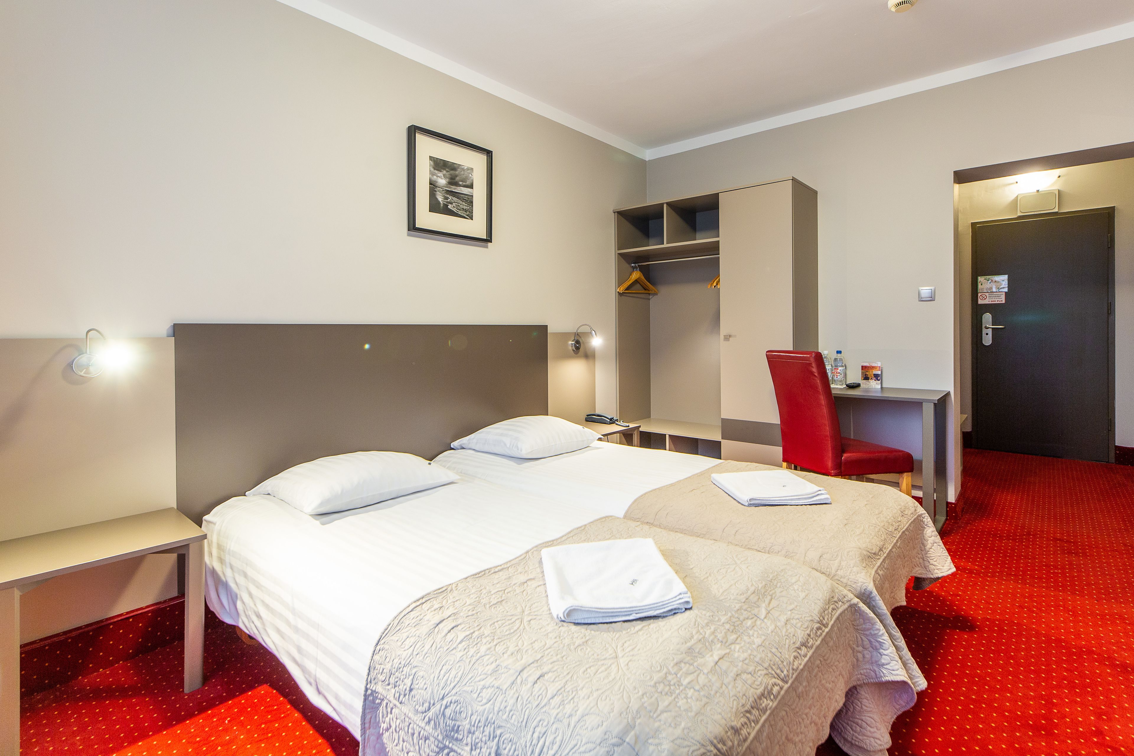 A hotel room with a large bed, a desk, a chair, and a wardrobe.
