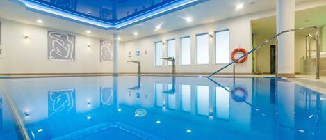 Una amplia piscina interior con agua cristalina azul, un salvavidas y un diseño arquitectónico moderno.