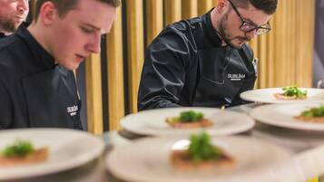 Chefs in black uniforms with 'Sublima Restaurant' on their jackets preparing dishes on plates.
