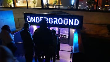 A sign for 'UNDERGROUND' with a modern design, located in an urban setting with visible architectural elements and a nighttime ambiance.