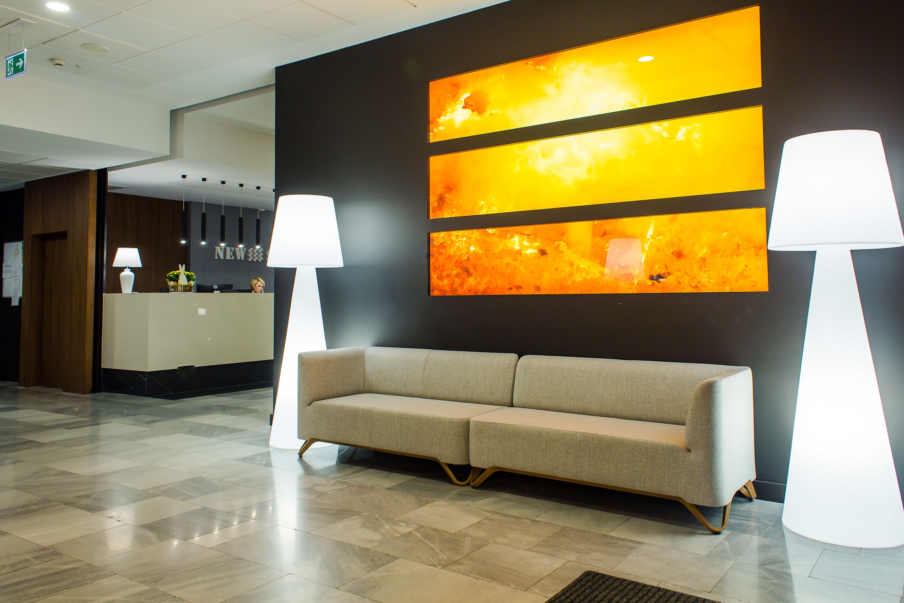 A reception area with a sofa, two lamps, and a wall with abstract art.