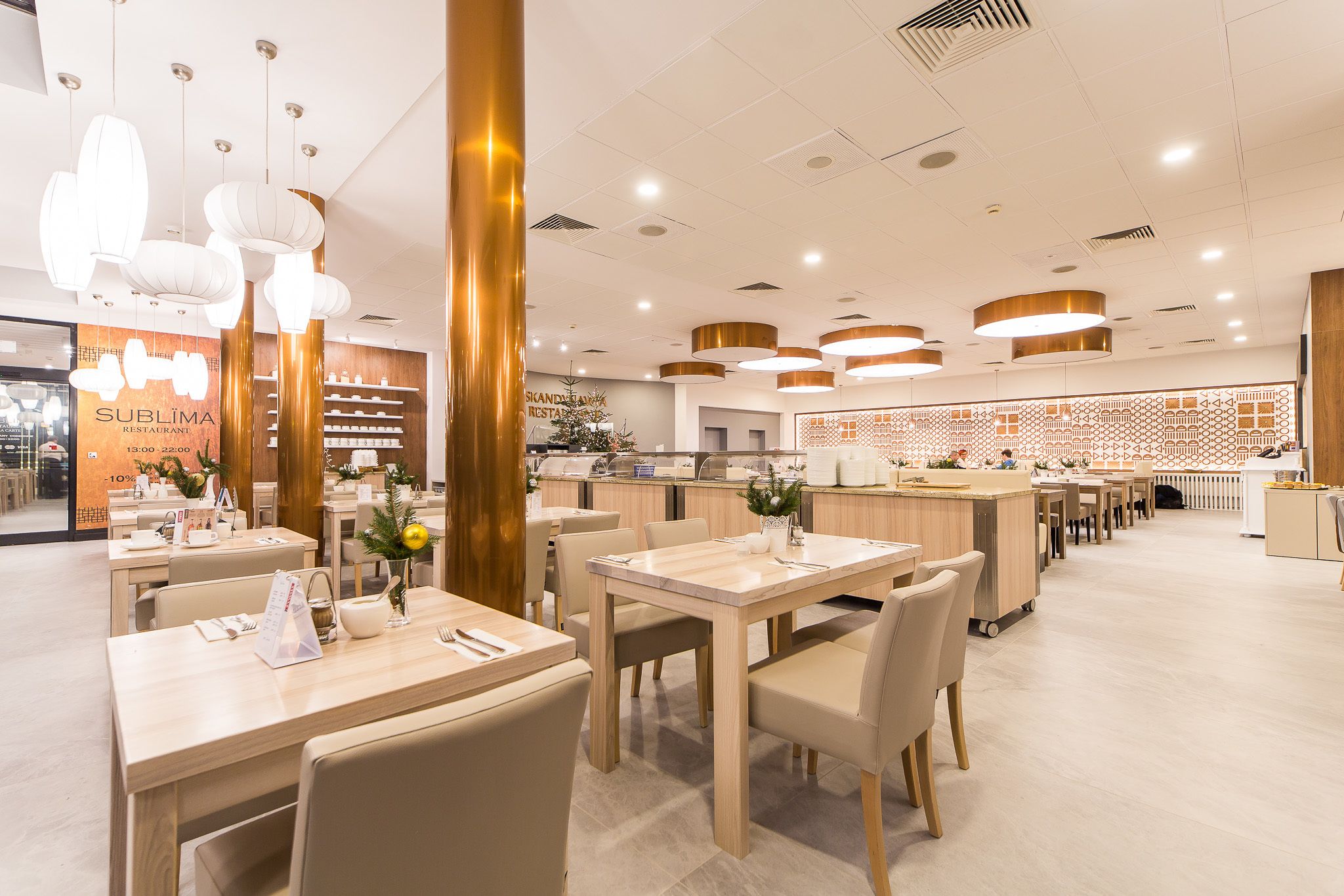 Un interior de restaurante moderno con mesas y sillas de madera, iluminación colgante y una pared decorativa.