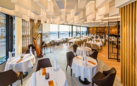 A modern restaurant with round tables, white tablecloths, and candle centerpieces.