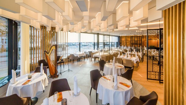 Een modern restaurant met ronde tafels, witte tafelkleden en kaarsdecoraties.