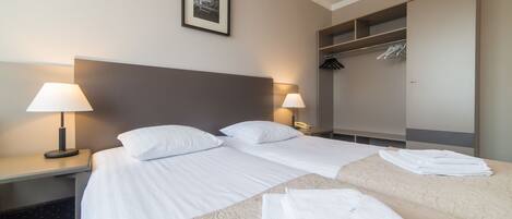 Habitación de hotel con dos camas, una mesita de noche con lámparas, un armario y un cuadro en la pared.