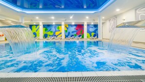 Piscina interna com vários jatos de água, painéis coloridos nas paredes e espreguiçadeiras.