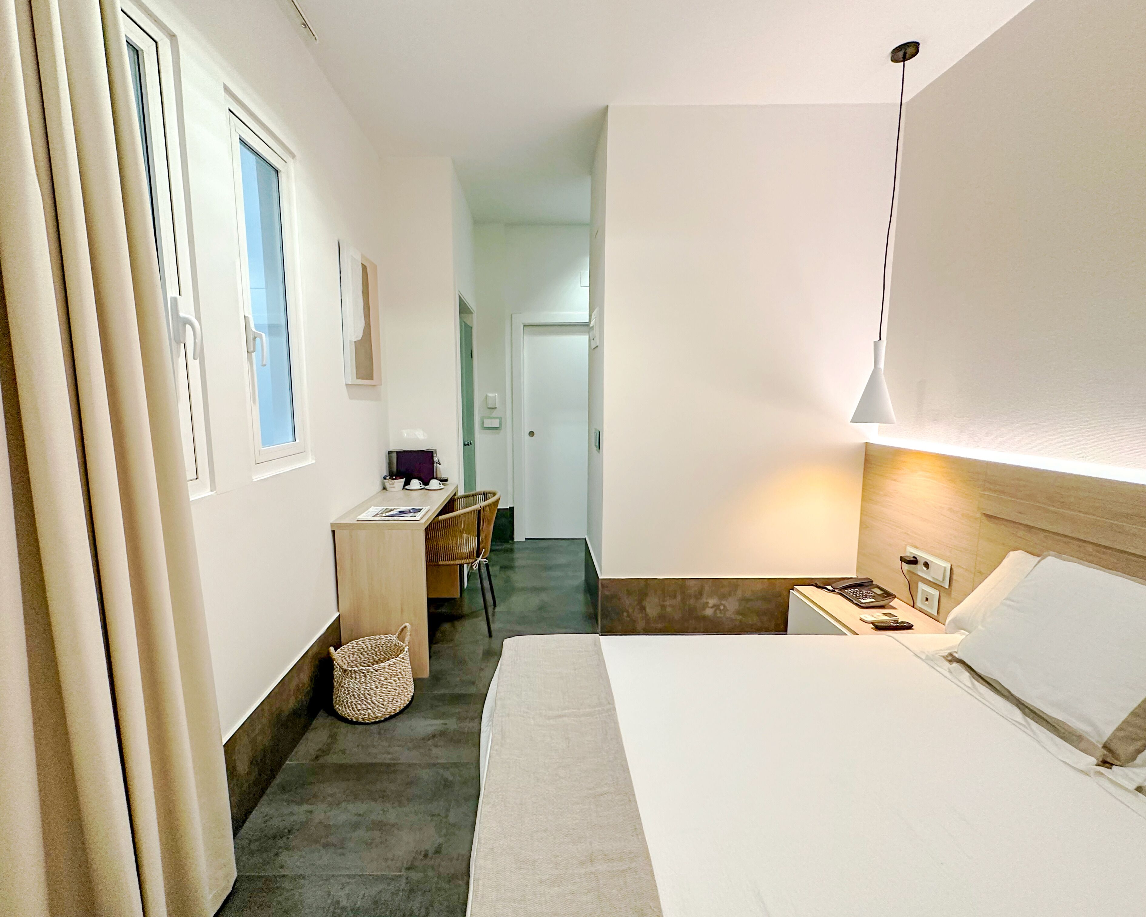 A hotel room with a bed, a desk, a chair, a lamp, and a window.