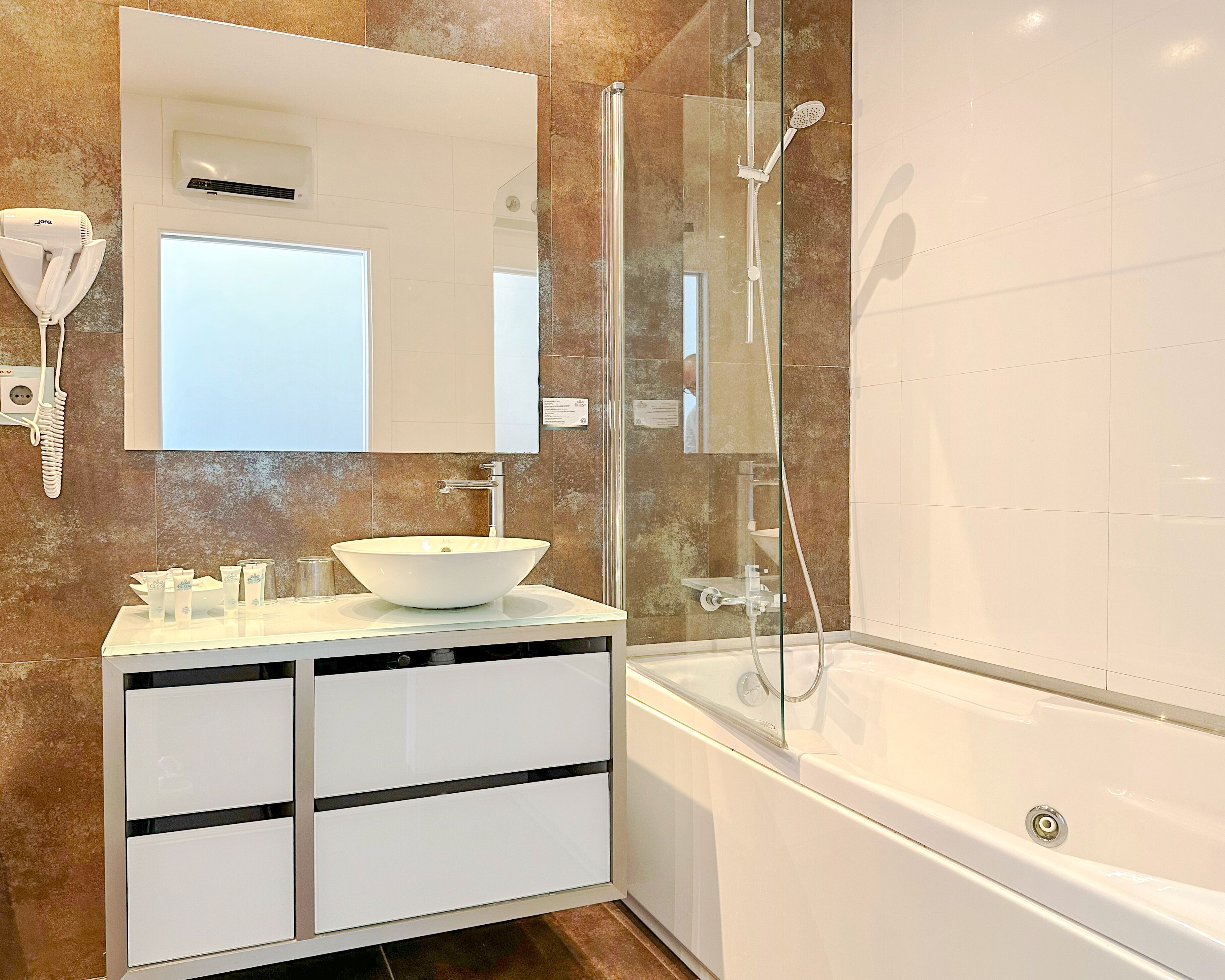 Un baño moderno con un lavabo blanco, un espejo grande, ducha con mampara de vidrio y una bañera blanca.