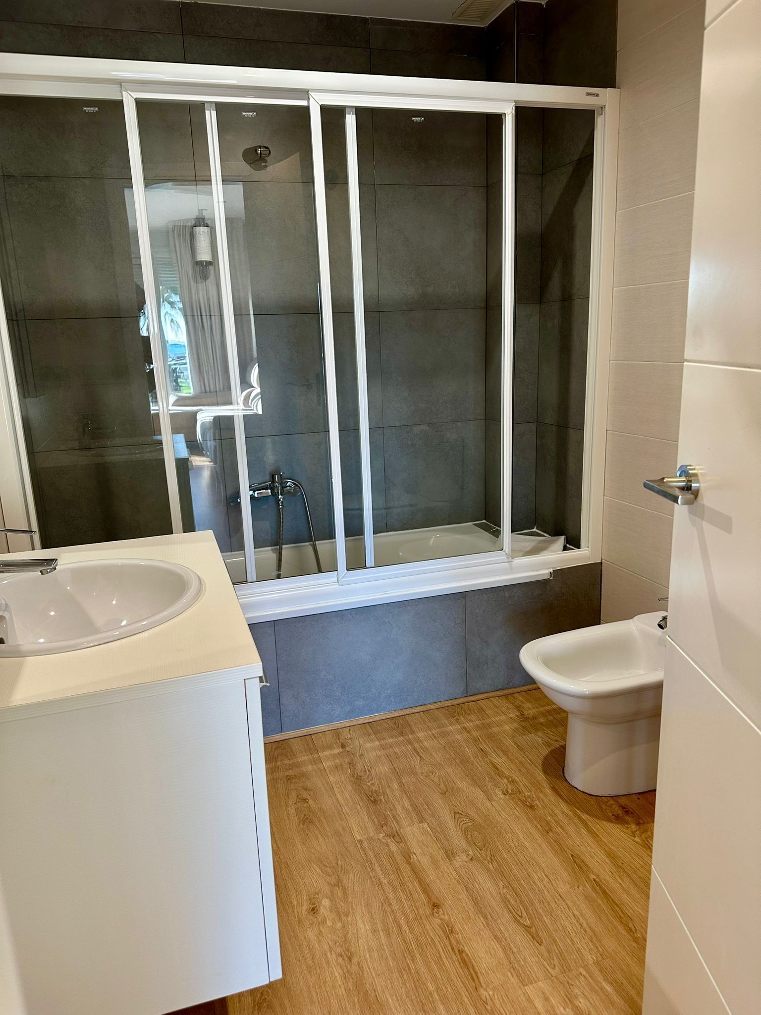 A modern bathroom with a glass-enclosed shower, a white sink, and a bidet.