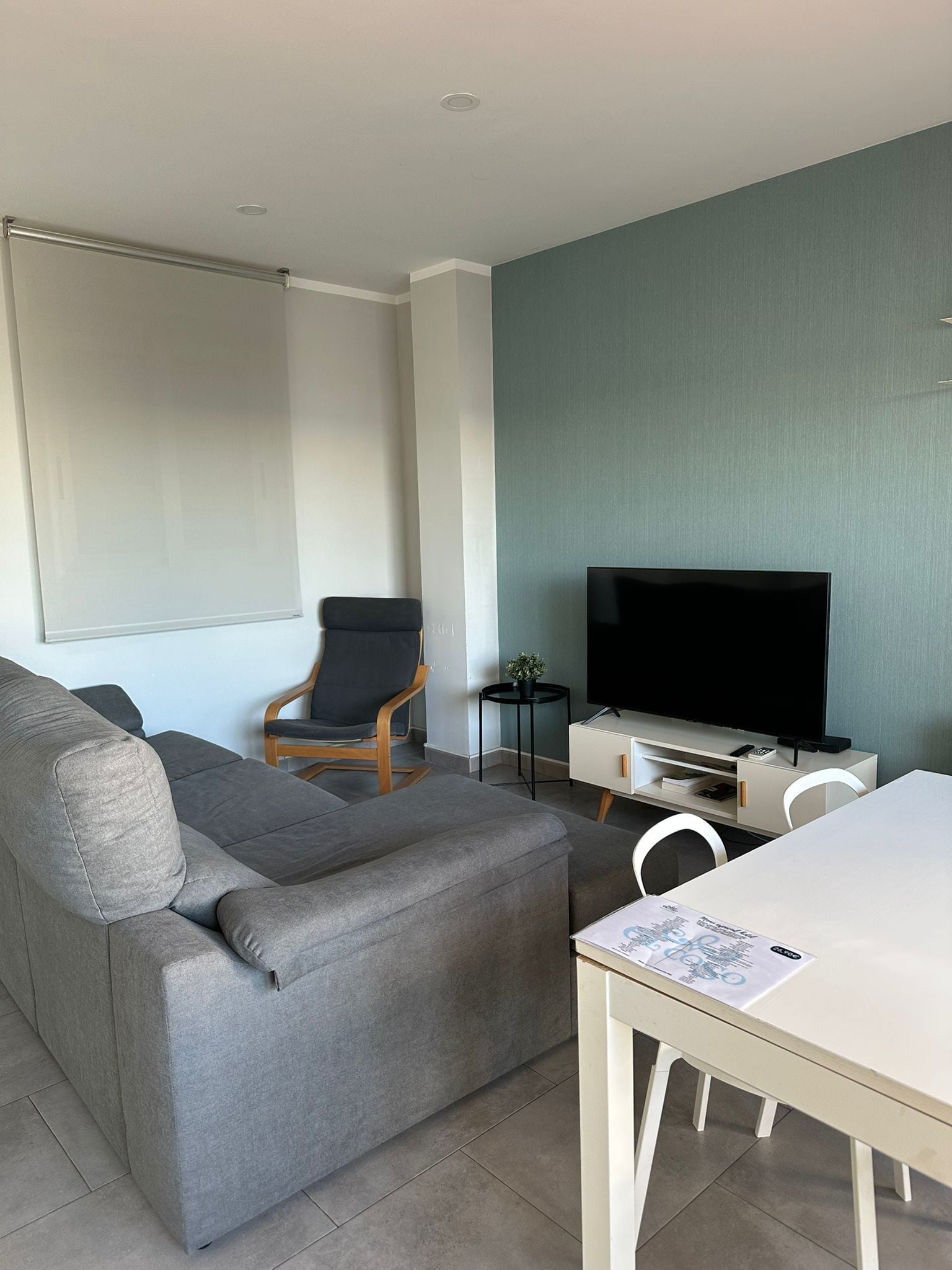 Un salon moderne avec un canapé gris, un petit fauteuil noir, un meuble TV blanc et une table à manger.