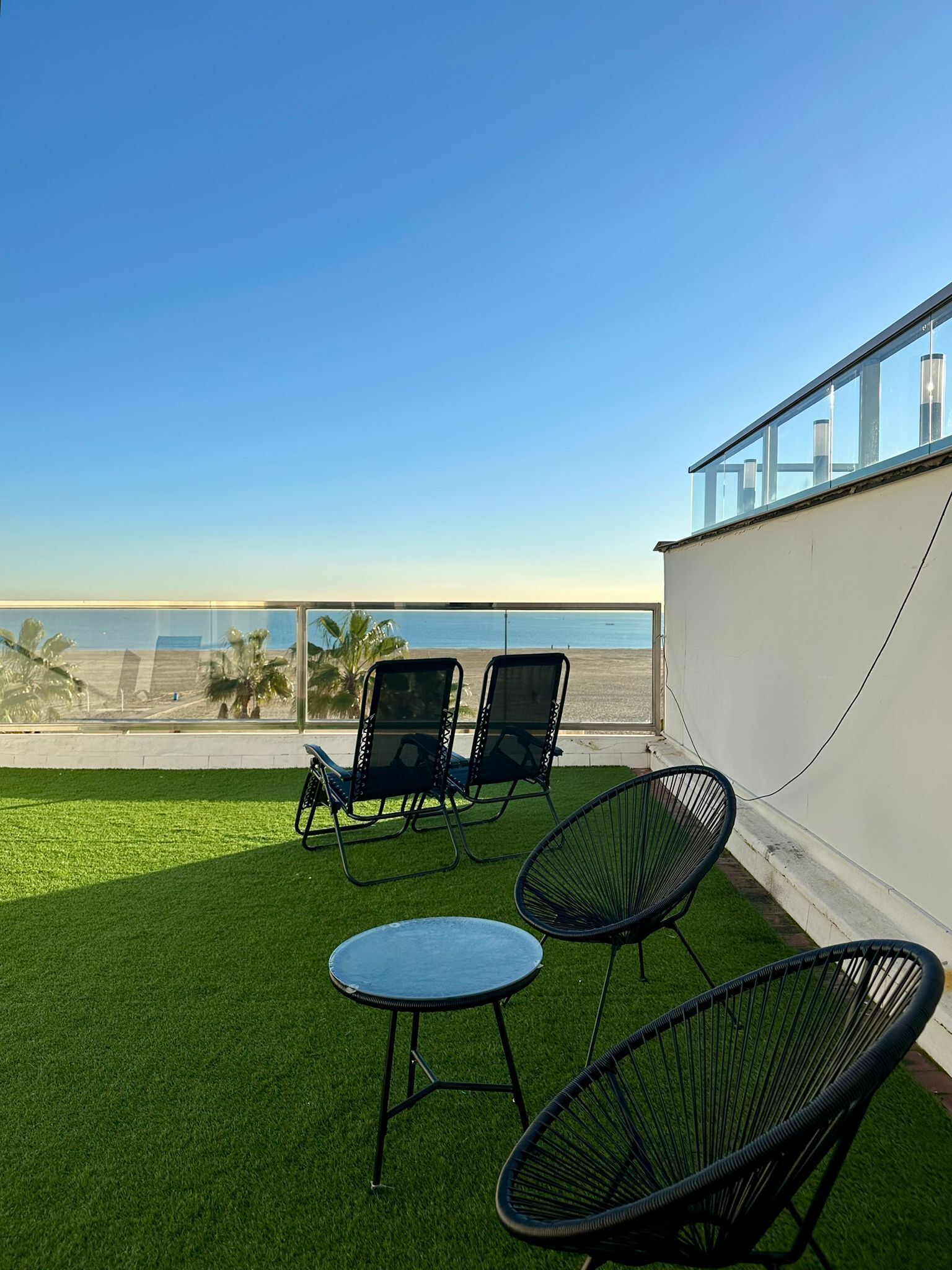 Un balcón con dos sillones de descanso y una pequeña mesa, con vista a la playa.
