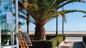 An outdoor dining area with a table set for two, a palm tree, and a view of the beach. - El Coso Hotel (Valencia)