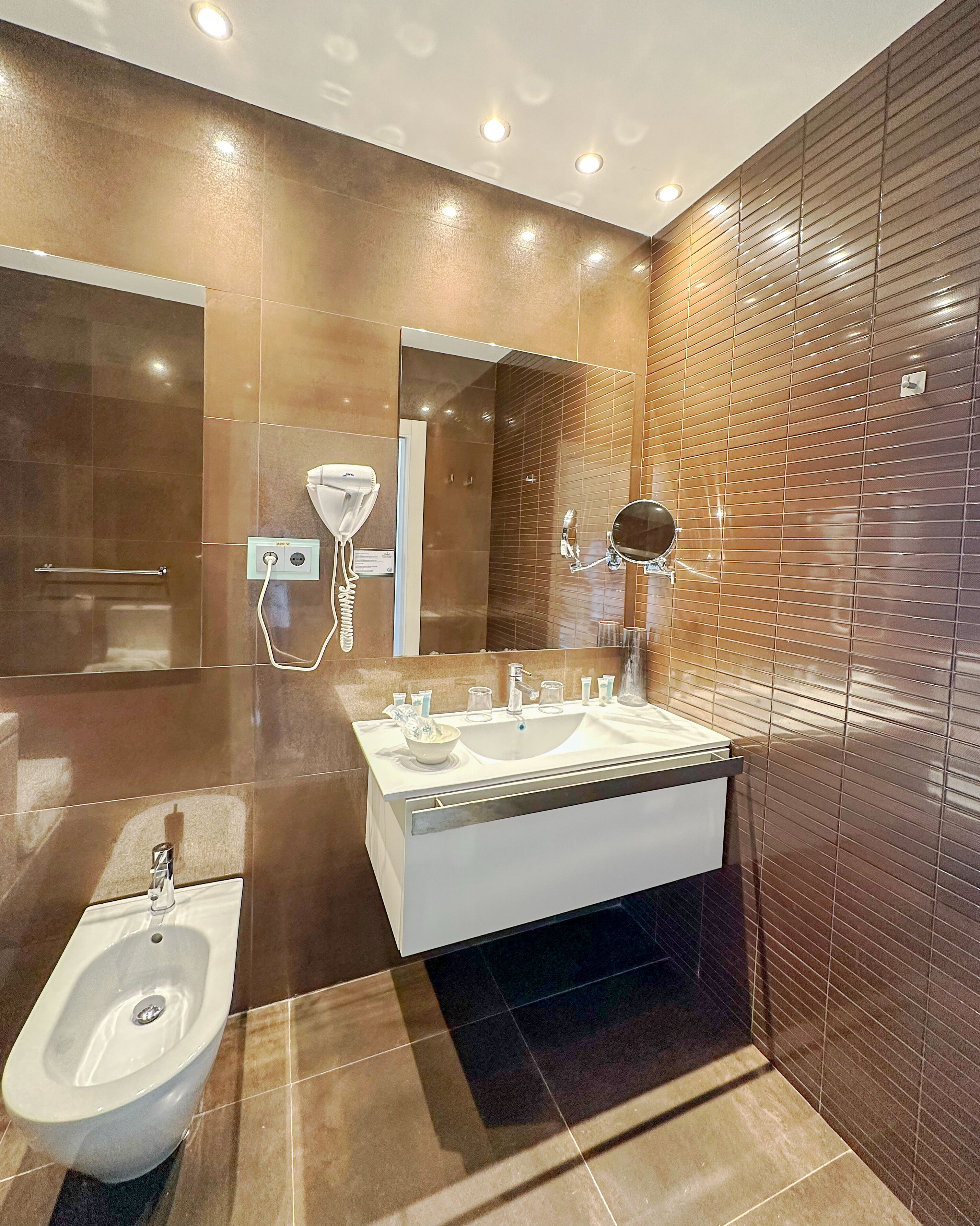 A modern bathroom with a large sink, a bidet, a mirror, and a hairdryer.