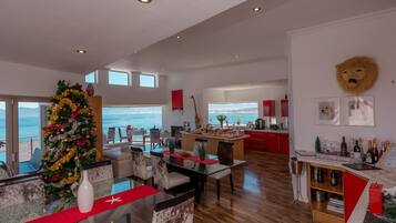 Un amplio salón con piso de madera, un árbol de Navidad y vista al océano.