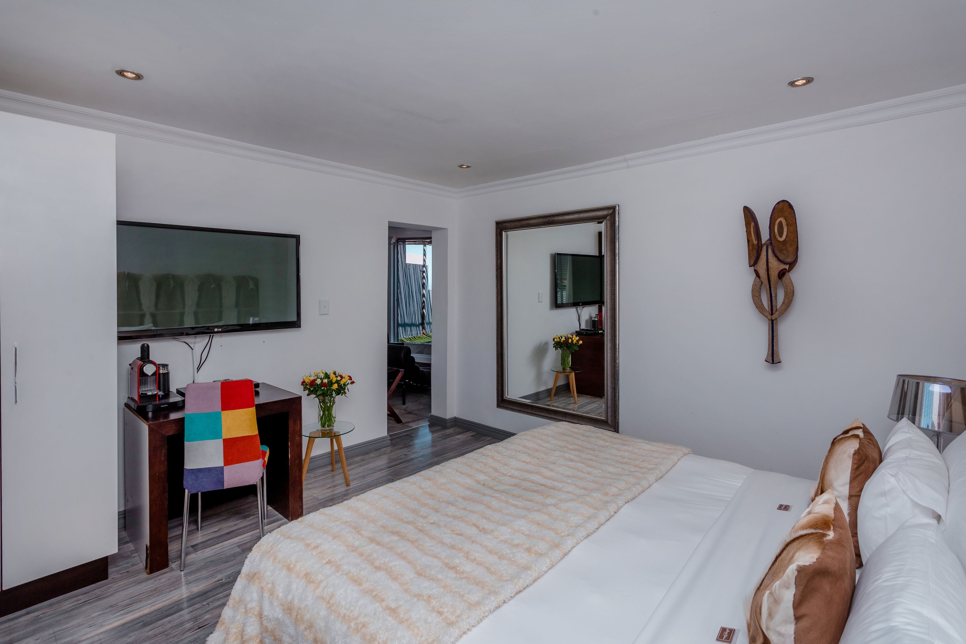 Quarto de hotel com cama grande, escrivaninha com cadeira, televisão e espelho.