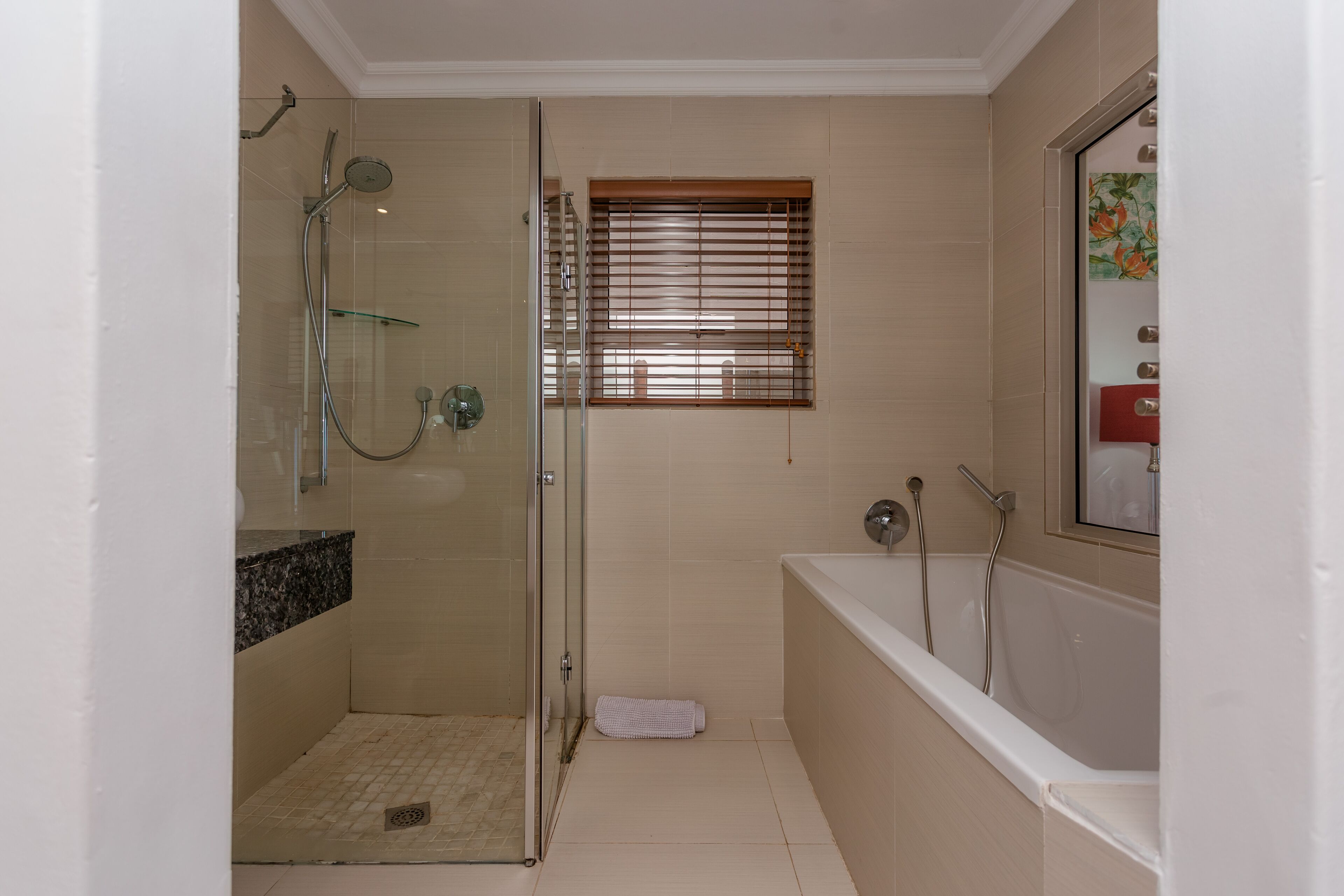 A bathroom with a glass-enclosed shower, a bathtub, and a window with blinds.