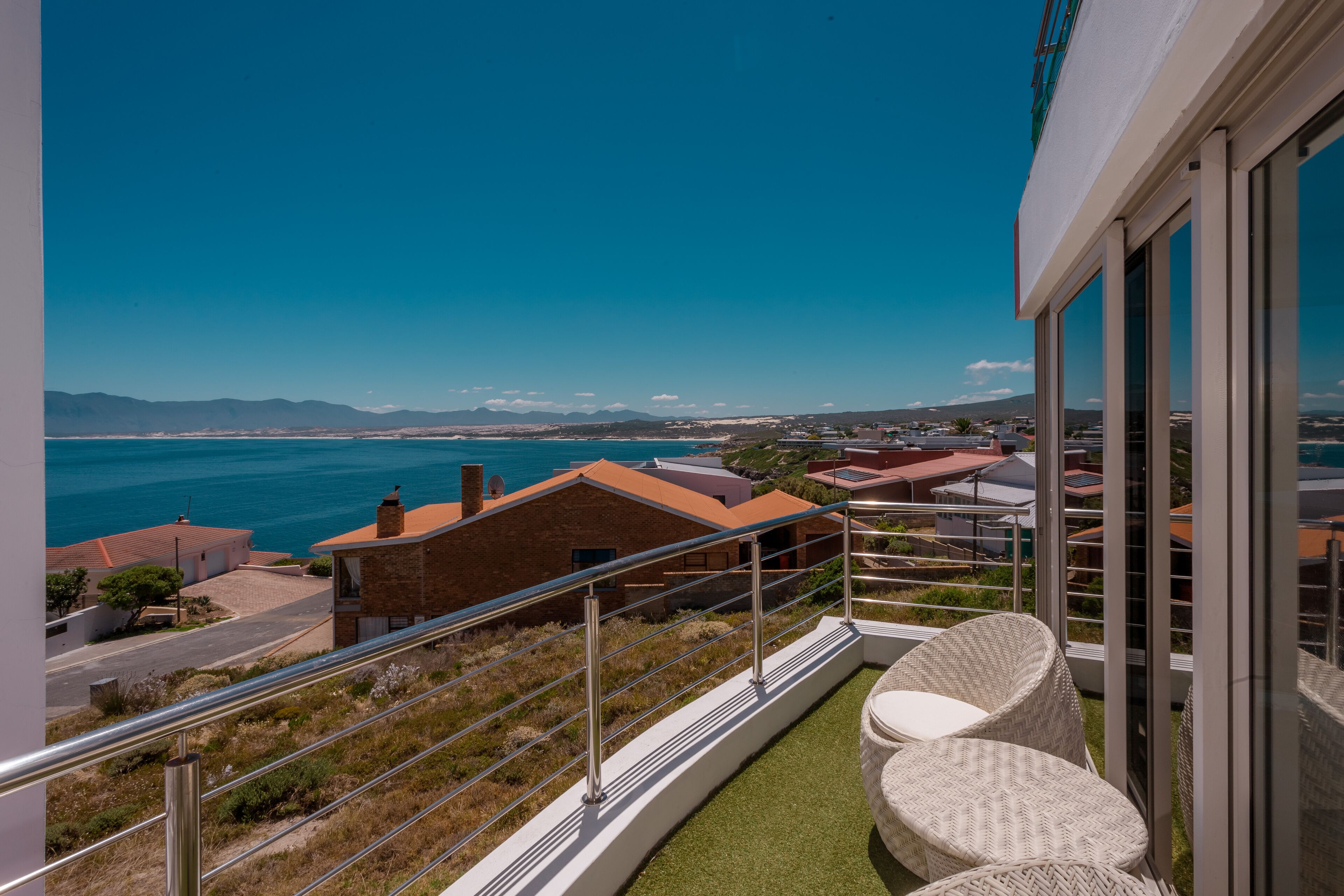Un balcon avec vue sur la mer, une pelouse et un bâtiment avec un toit rouge.