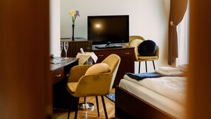 A hotel room with a bed, a desk with a television, a chair, and a small table with a vase of flowers. - Korona Pension Restaurant (Hévíz)