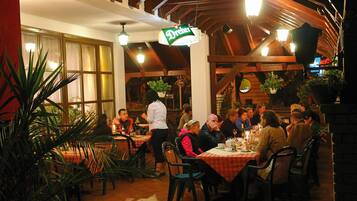 Een terras met tafels en stoelen, een bord met daarop een restaurantnaam, en potplanten eromheen.