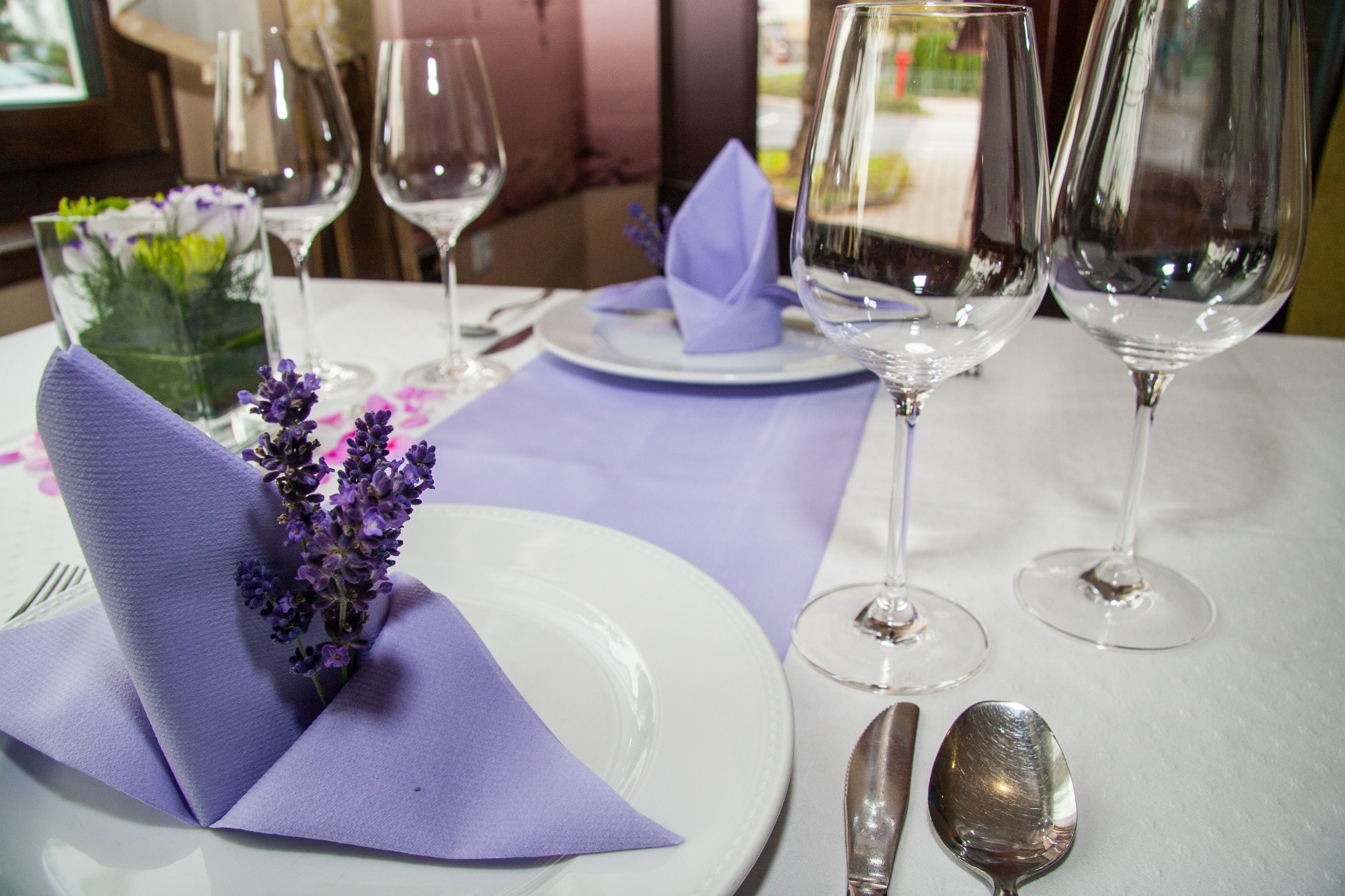 A table set with white plates, purple napkins, and clear wine glasses.