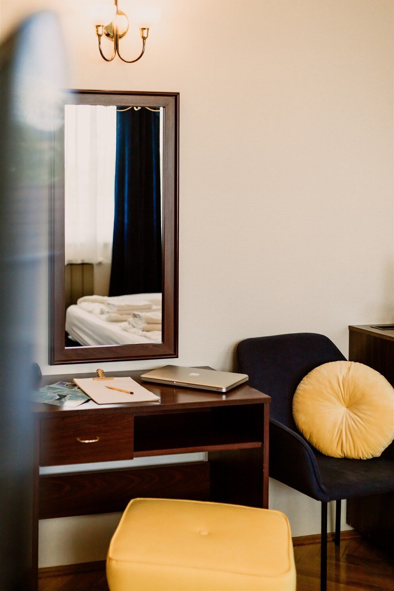 A hotel room with a wooden desk, a laptop, a notebook, and a chair with a yellow cushion.