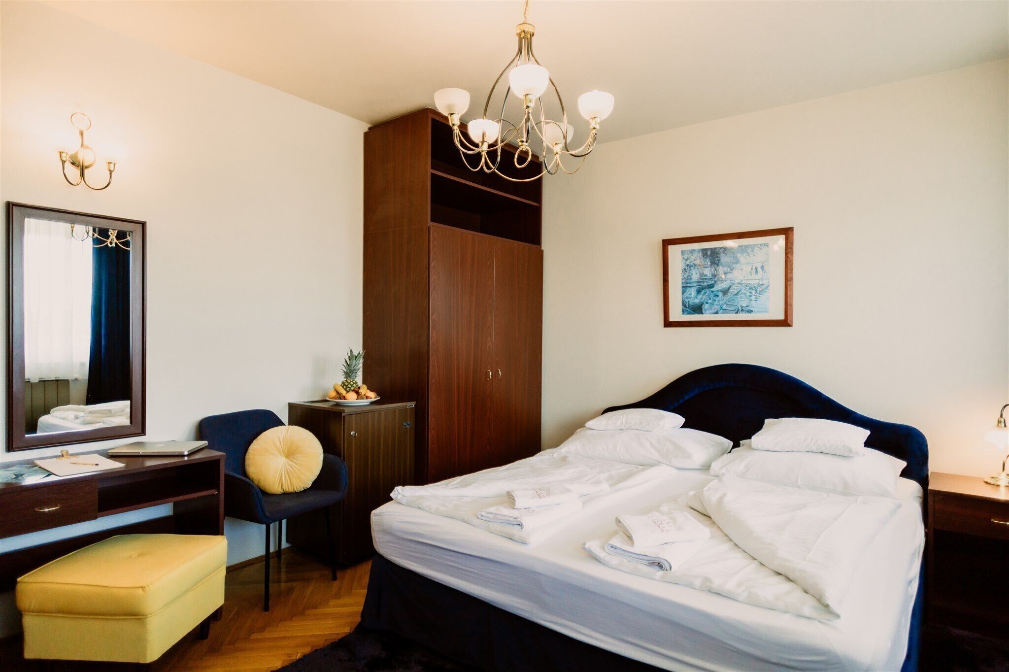 Ein Hotelzimmer mit einem großen Bett, einem Schreibtisch mit Stuhl, einem Kleiderschrank, einem Spiegel und einer Kandelaber.