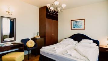 Ein Hotelzimmer mit einem großen Bett, einem Schreibtisch mit Stuhl, einem Kleiderschrank, einem Spiegel und einer Kandelaber.
