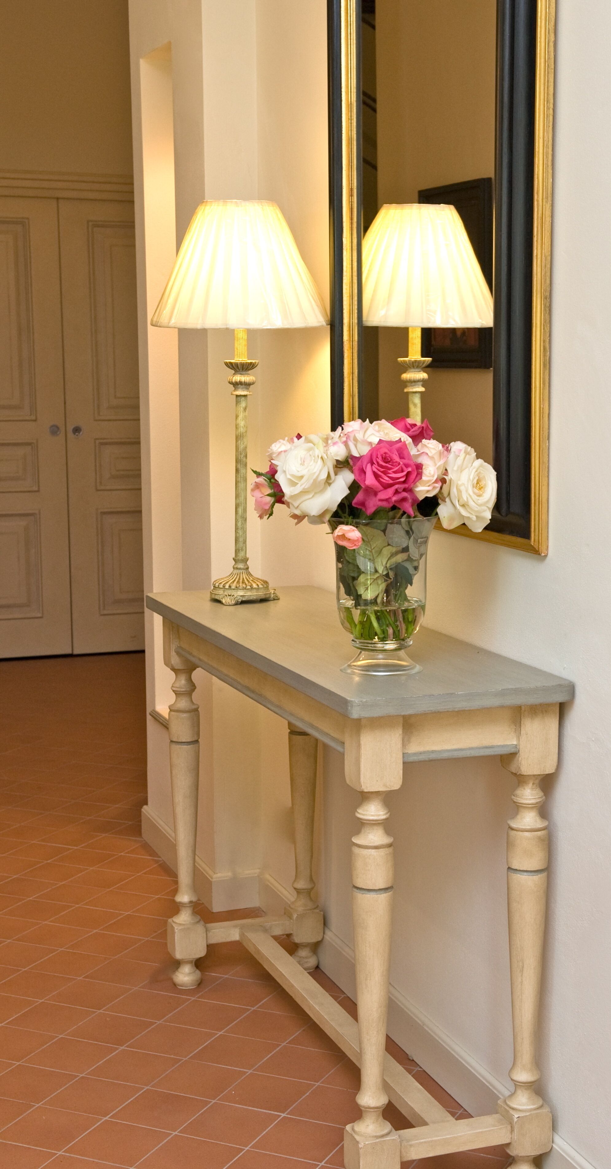 Een hal met een console tafel, twee lampen, een bloemenvaas en een spiegel.