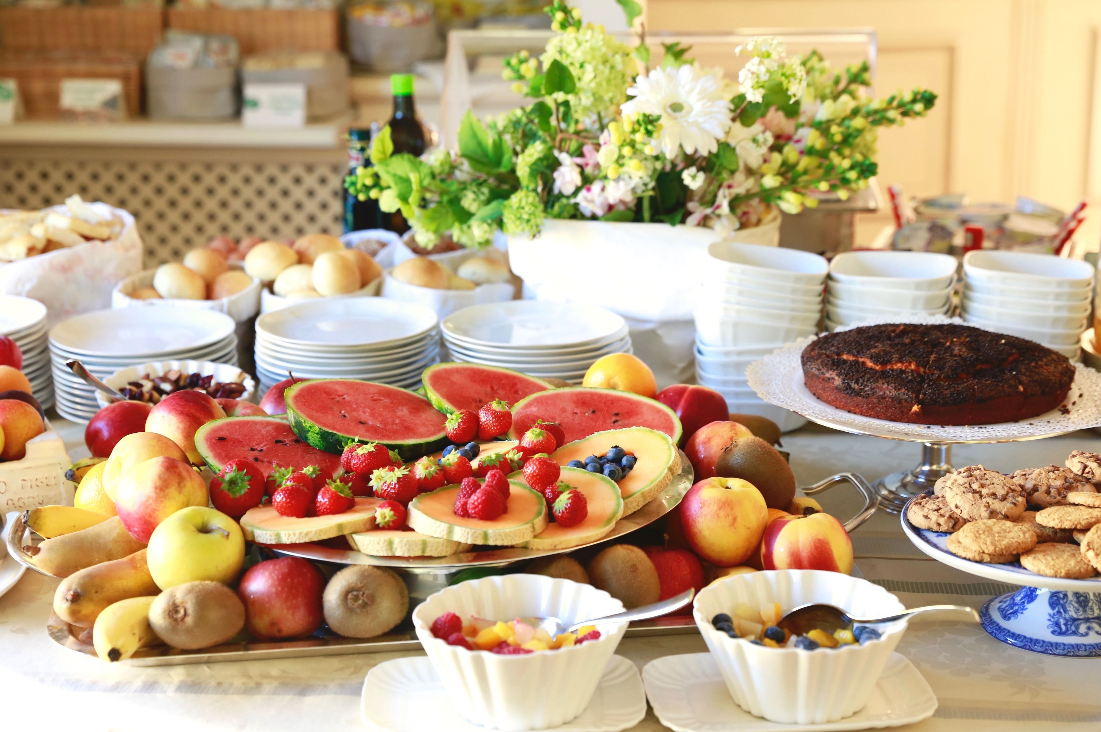 Una mesa de buffet con diversas frutas, un pastel y platos apilados.