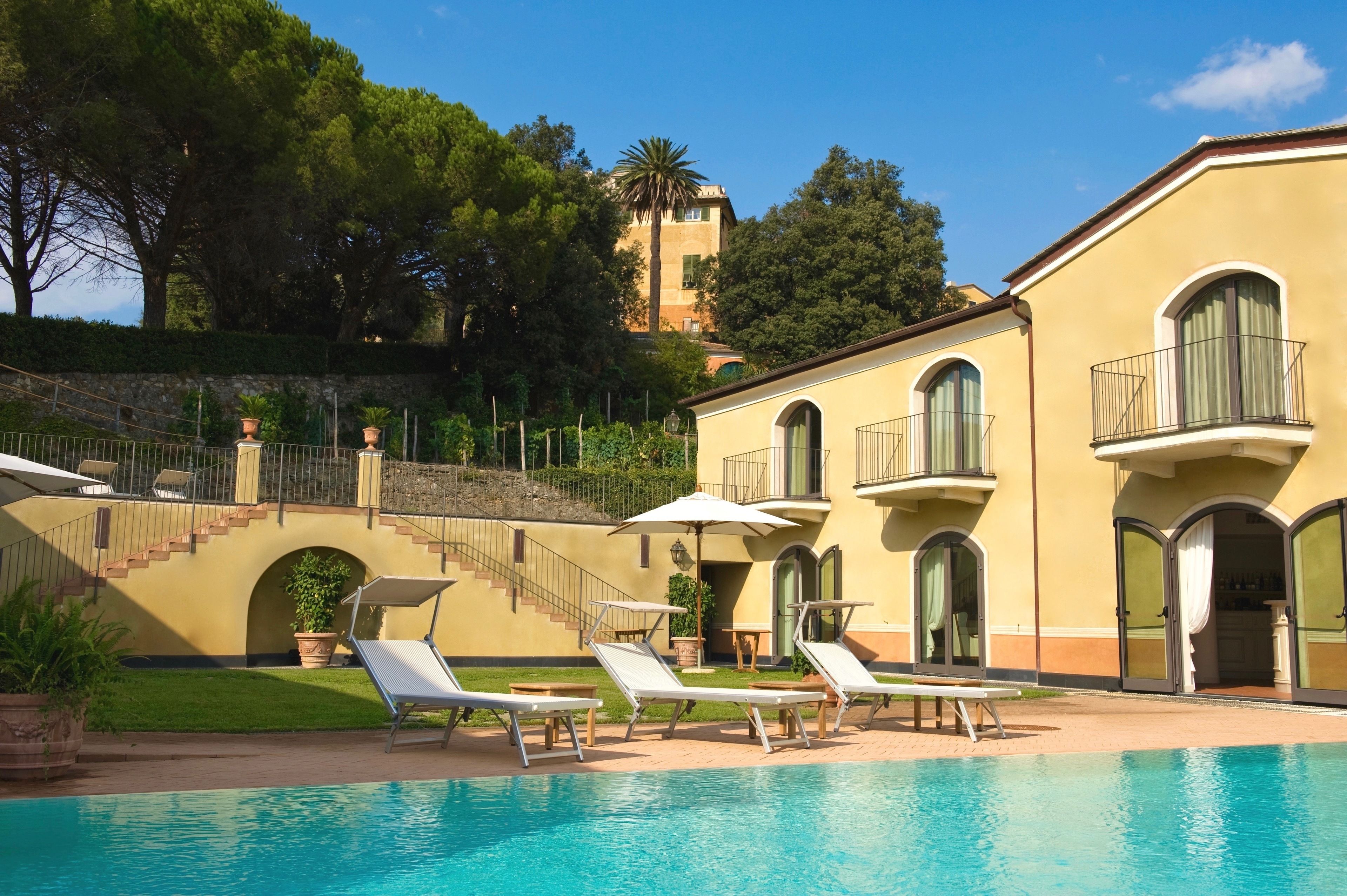 Un espace aménagé au bord de la piscine, avec des chaises longues, un escalier et un bâtiment doté de fenêtres en arc de cercle et de balcons.